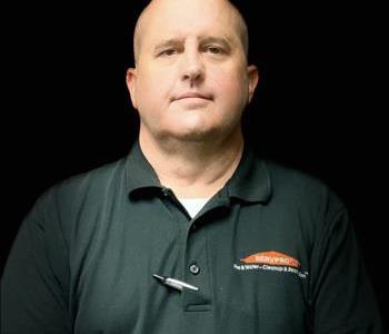 male wearing an all black shirt with SERVPRO logo in orange.He has a pen by the buttons in the shirt.